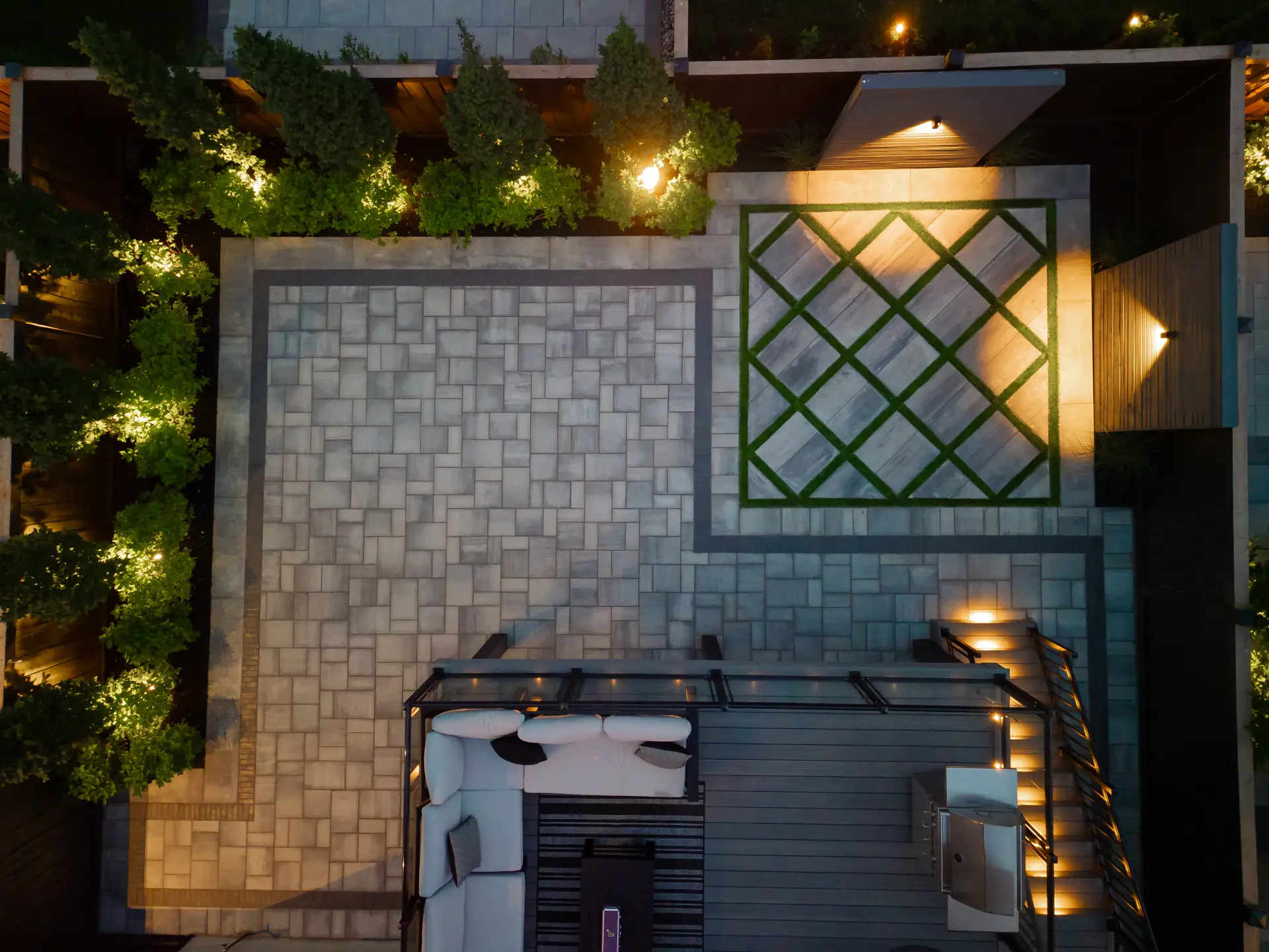 Backyard pool surrounded by a large-format paver patio with landscape lighting at dusk