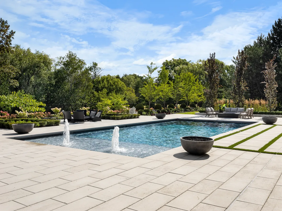 Large-format interlocking slab patio with grass joint bands surrounding a pool with fountains