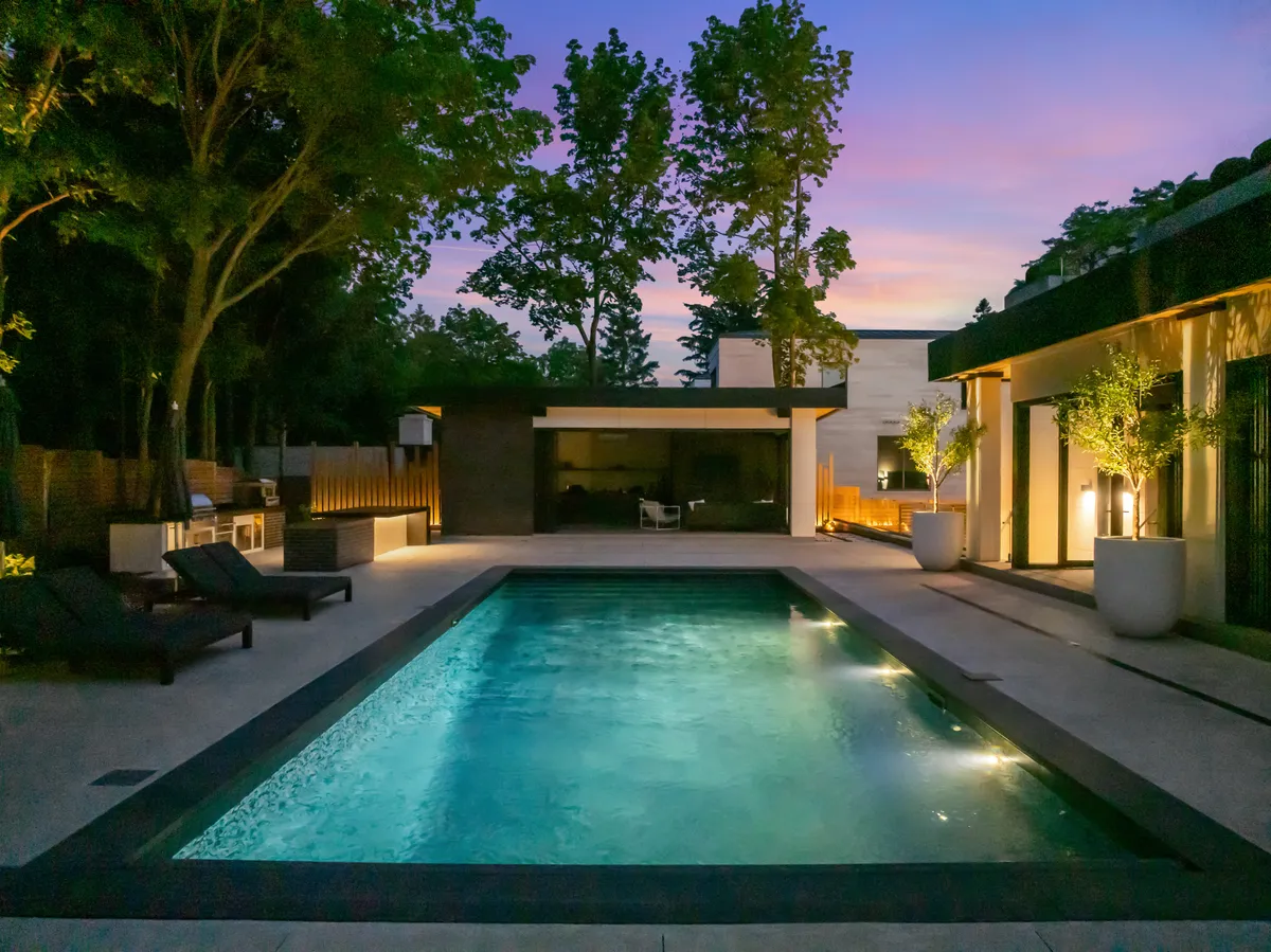 Backyard pool and cabana illuminated by layered landscape lighting at dusk