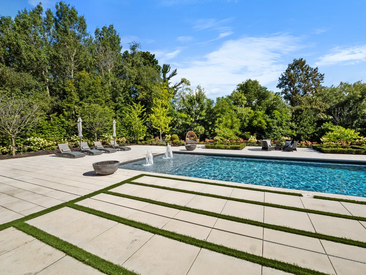 Large-format pavers with grass joints and fountain jets beside a luxury pool