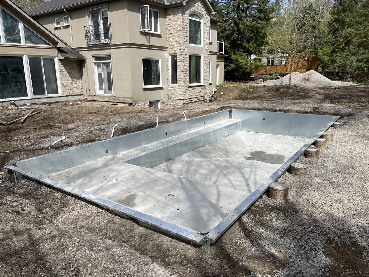 New steel pool wall structure installed in an excavated backyard behind an Ontario home