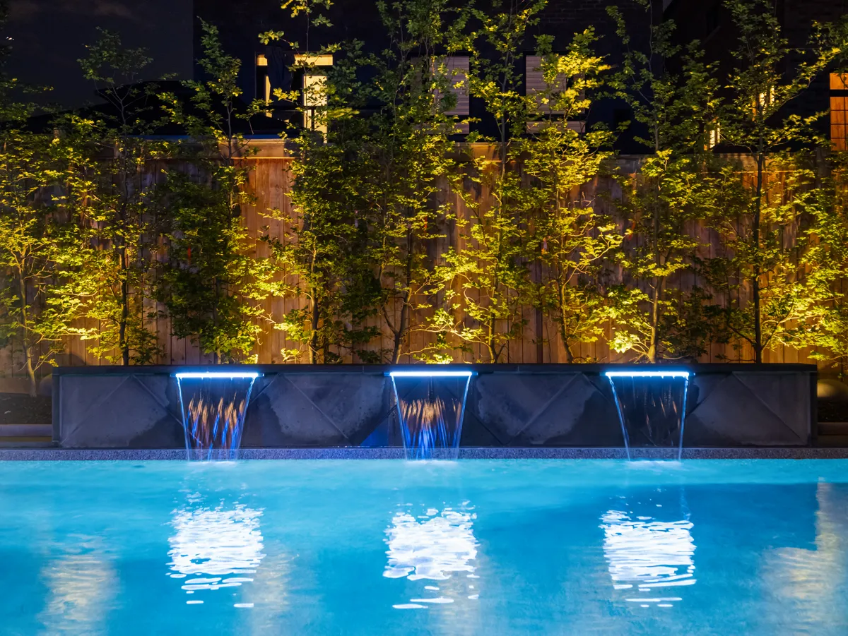 Illuminated waterfall water features spilling into a pool at night with landscape lighting