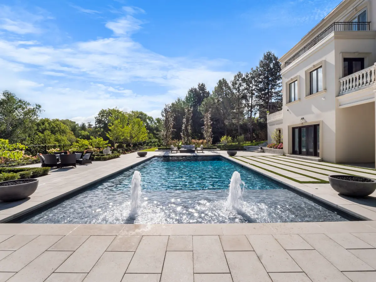 Custom pool with two bubbler jets, large-format pavers and a terrace lounge beside a stone home