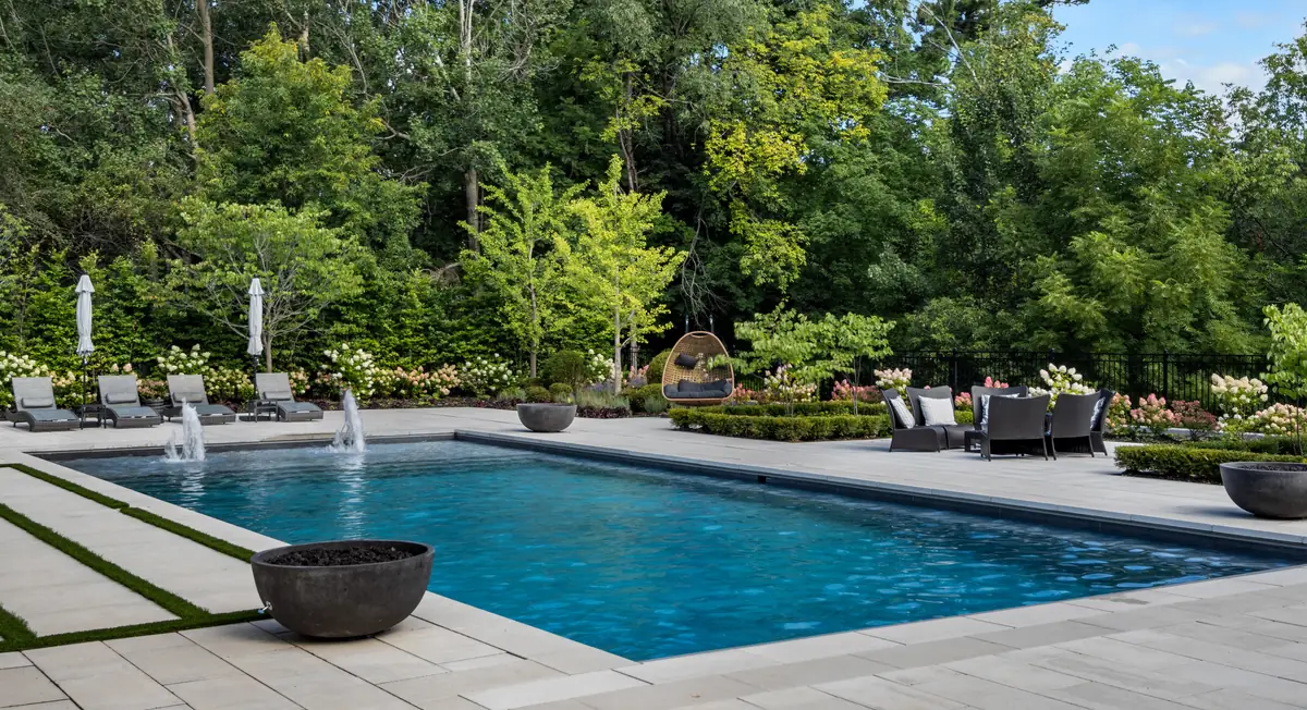 Rectangular pool with fountain bowls, lounge chairs, a porcelain patio and planted gardens designed and built as one backyard