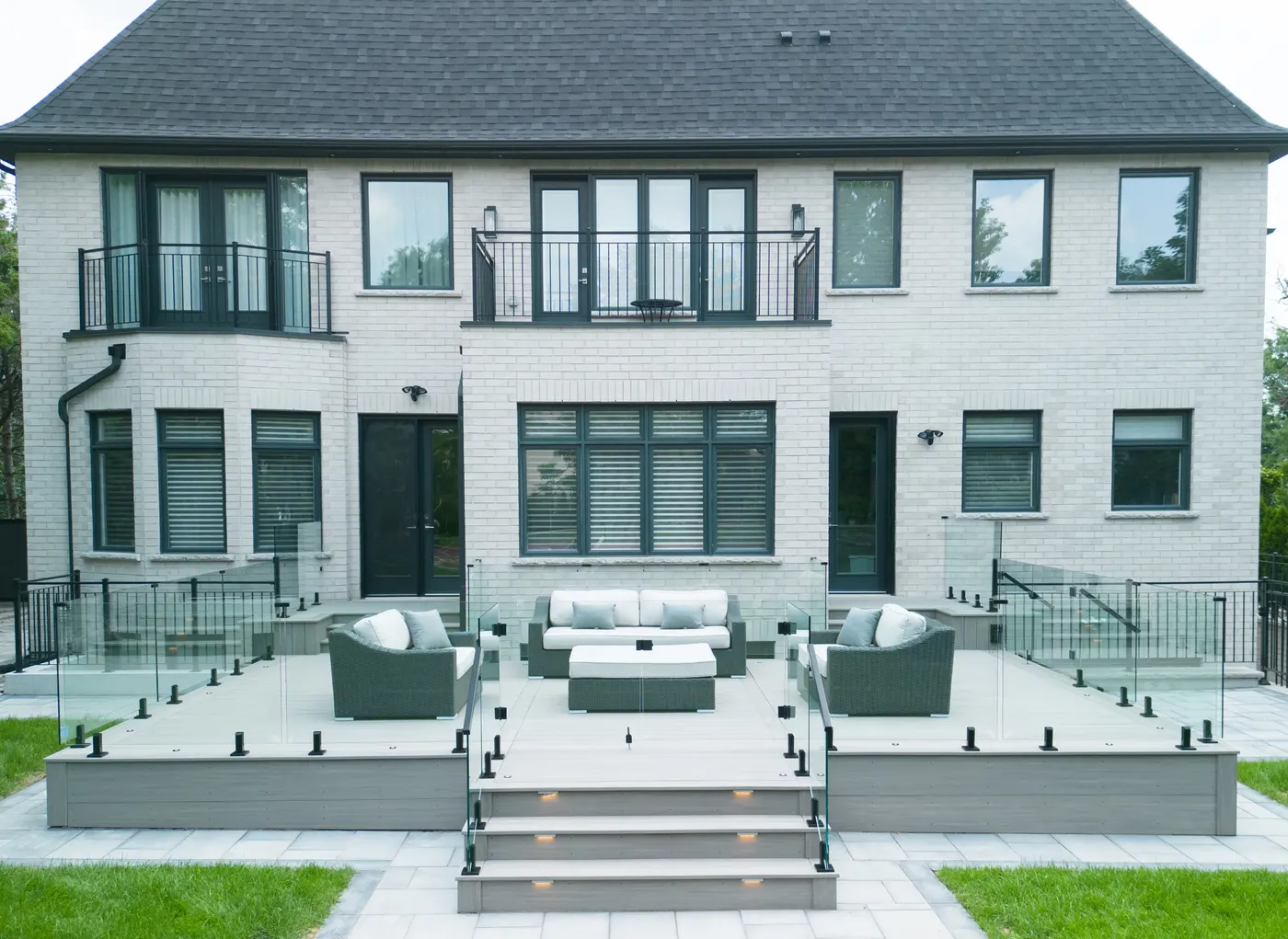 Multi-level composite deck with frameless glass railings and lit steps behind a brick home