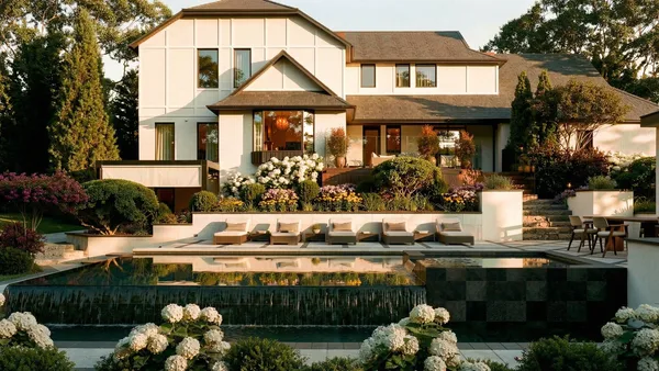 Brule landscape design render &mdash; Infinity-edge pool head-on at golden hour, the lit house and planted terraces reflected in the water