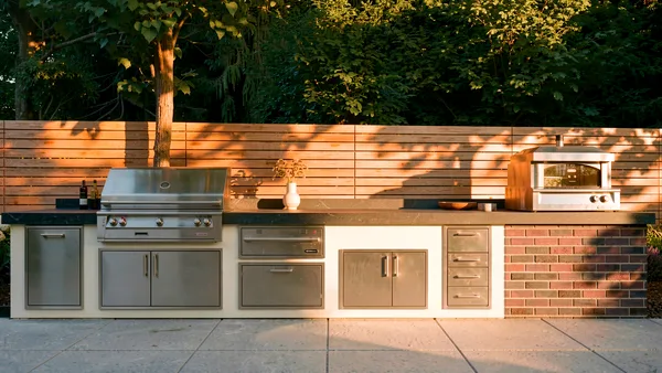 Waymar custom outdoor kitchen run &mdash; grill, pizza oven and brick cabinetry against the wood privacy fence