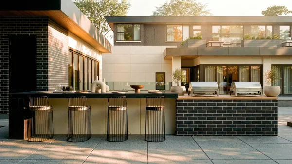 Waymar outdoor kitchen bar at dusk &mdash; brick island with counter stools beside the house