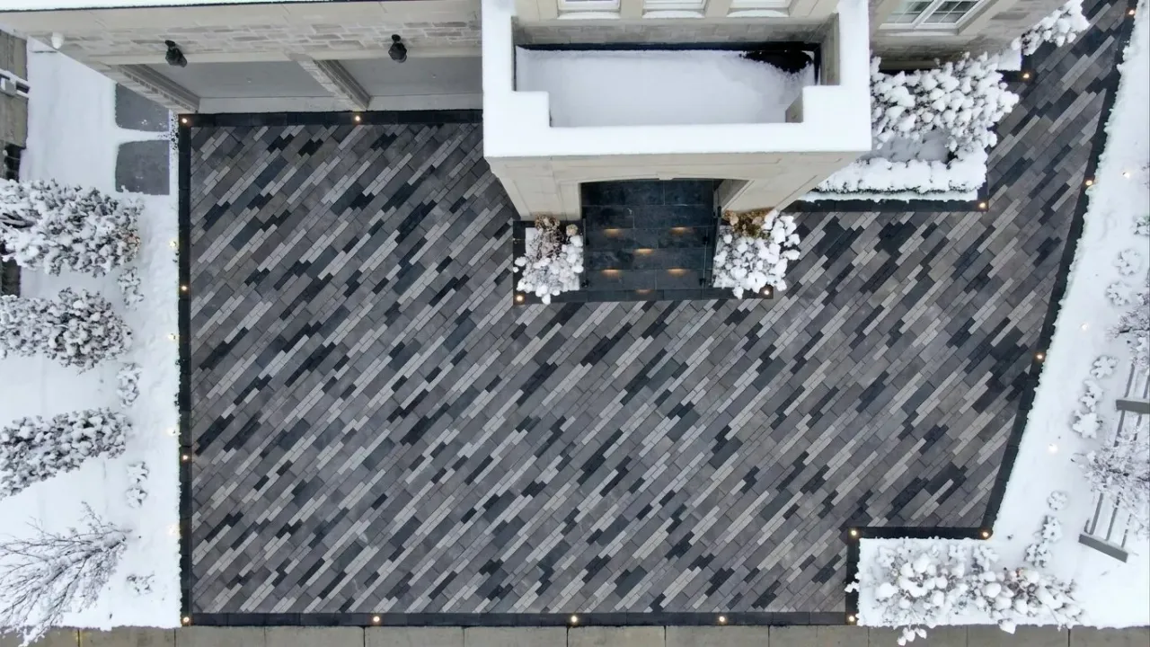 Heated driveway with pavers clear of snow while the surrounding yard stays snow-covered
