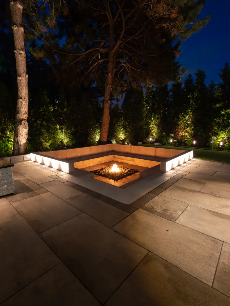Sunken stone fire pit lounge lit at night beneath tall pines