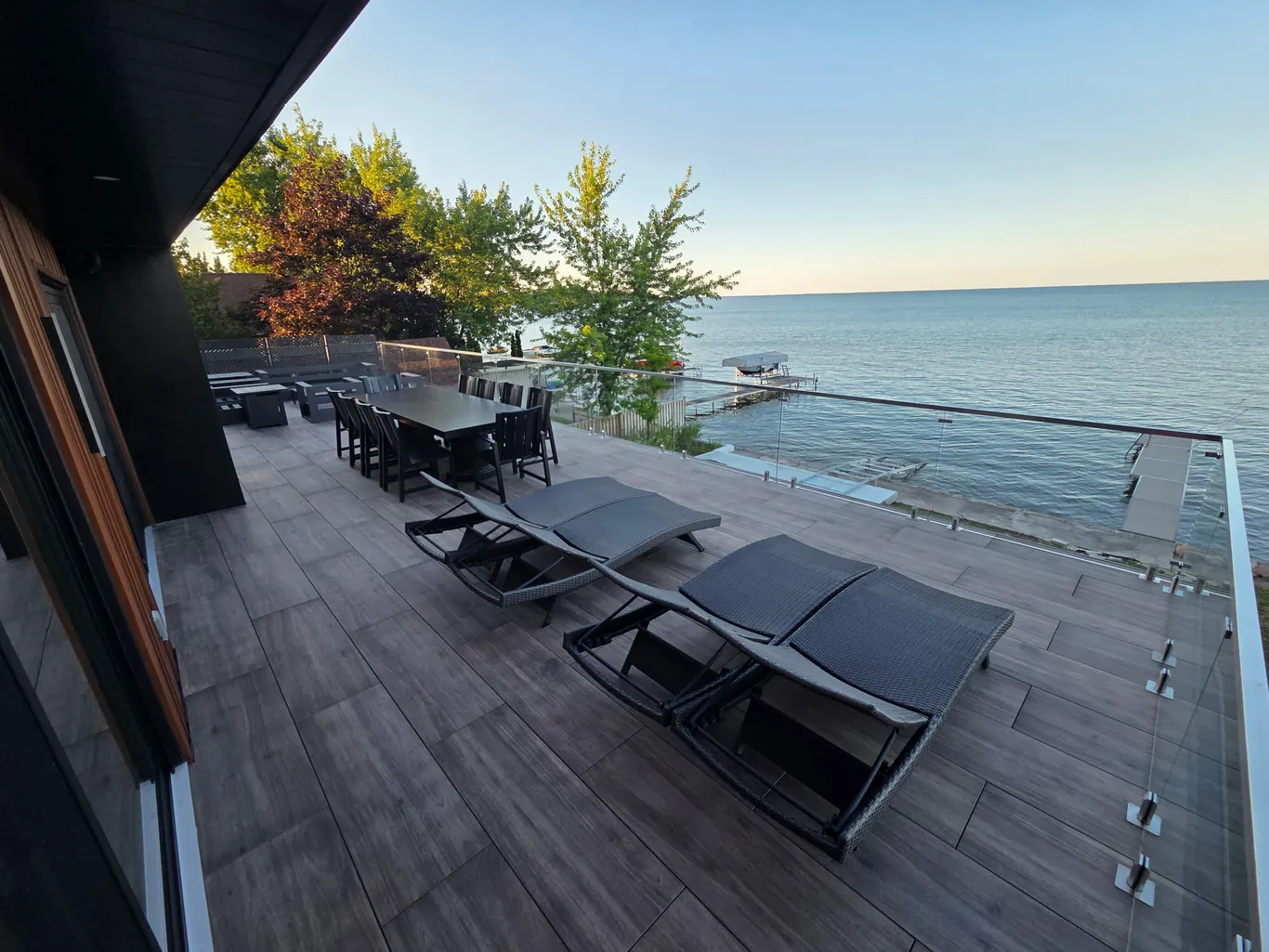 Waterfront deck with glass railings, outdoor dining and lounge chairs overlooking the lake