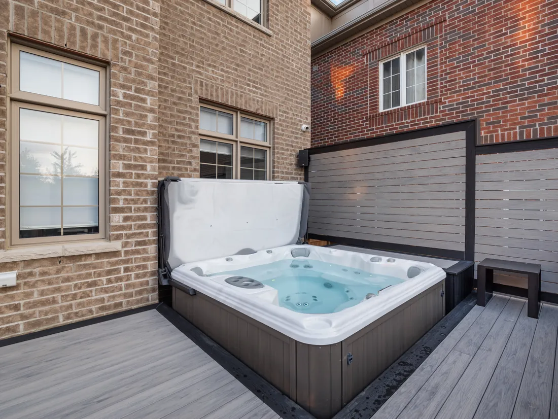 Hot tub recessed into a composite deck with a privacy screen between brick walls