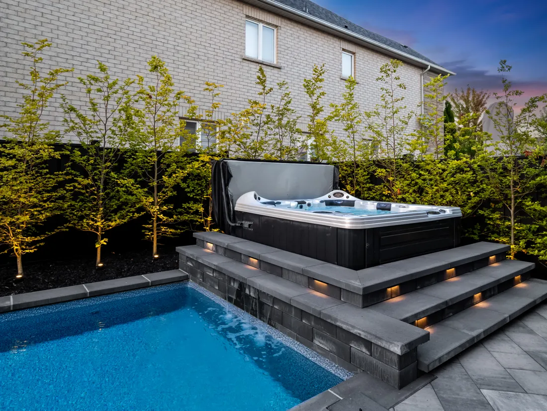 Elevated hot tub on stone steps with a waterfall spilling into a backyard pool