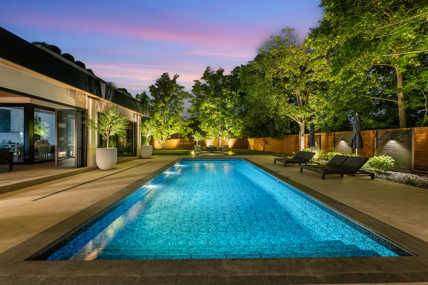 Rectangular inground pool with underwater lighting and uplit trees at dusk